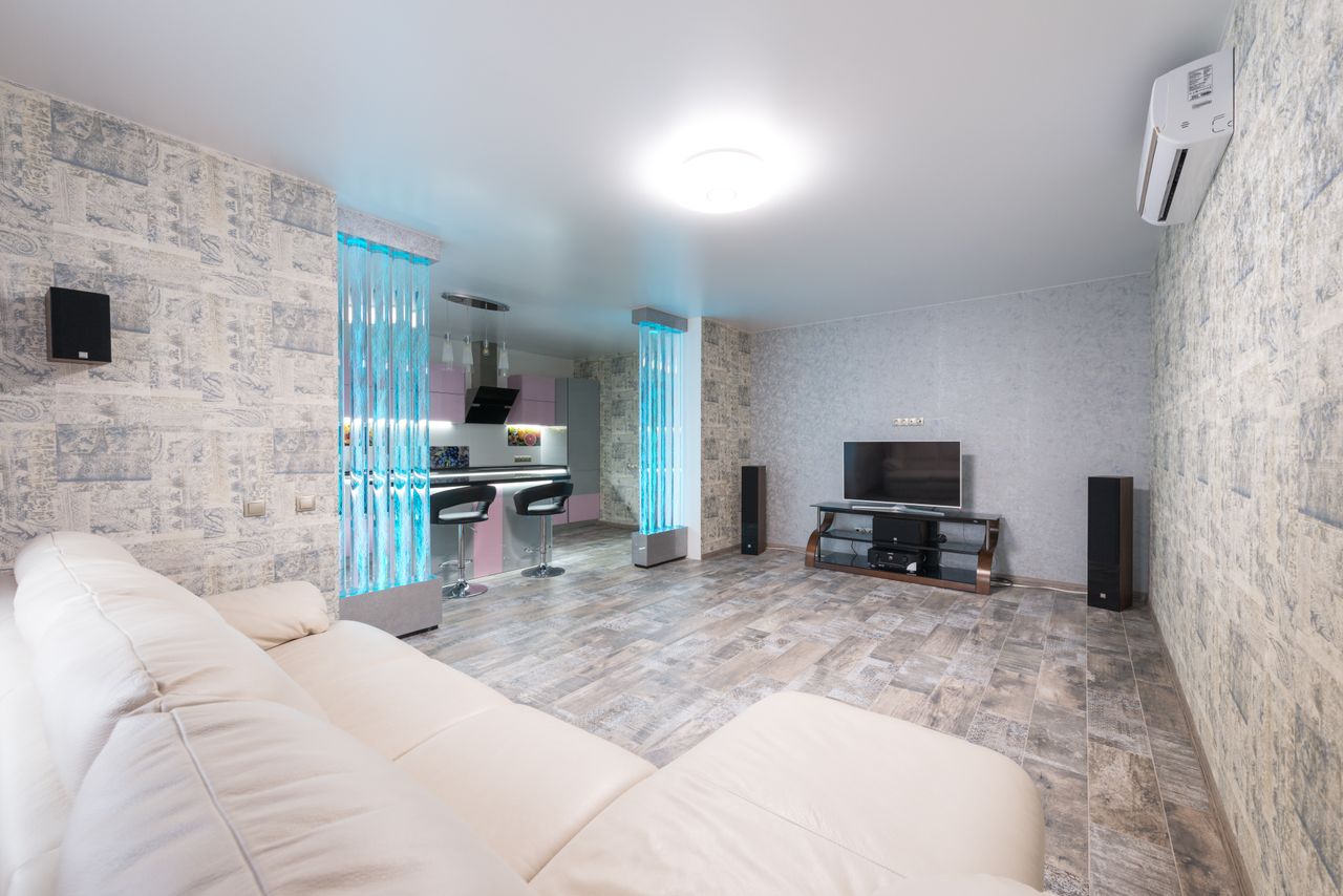 Comfortable white sofa placed in spacious room with TV and decorative colorful bubble wall near modern kitchen in stylish apartment